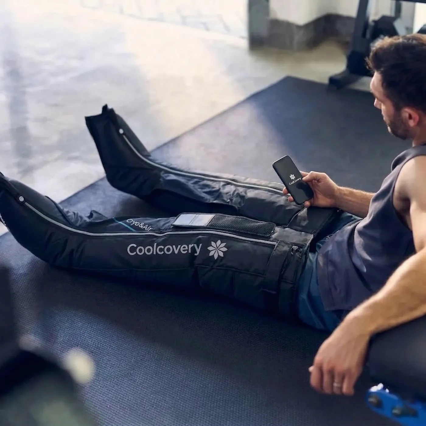 A man resting in CoolCovery compression boots, checking his phone.